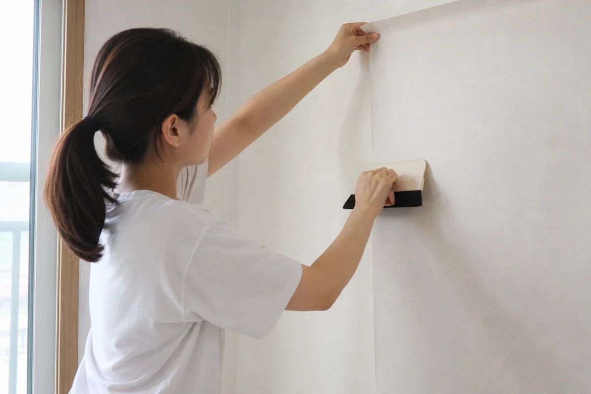 작은 방에서 벽지 이음매를 맞추고 정배솔로 기포를 제거하는 셀프도배 모습
