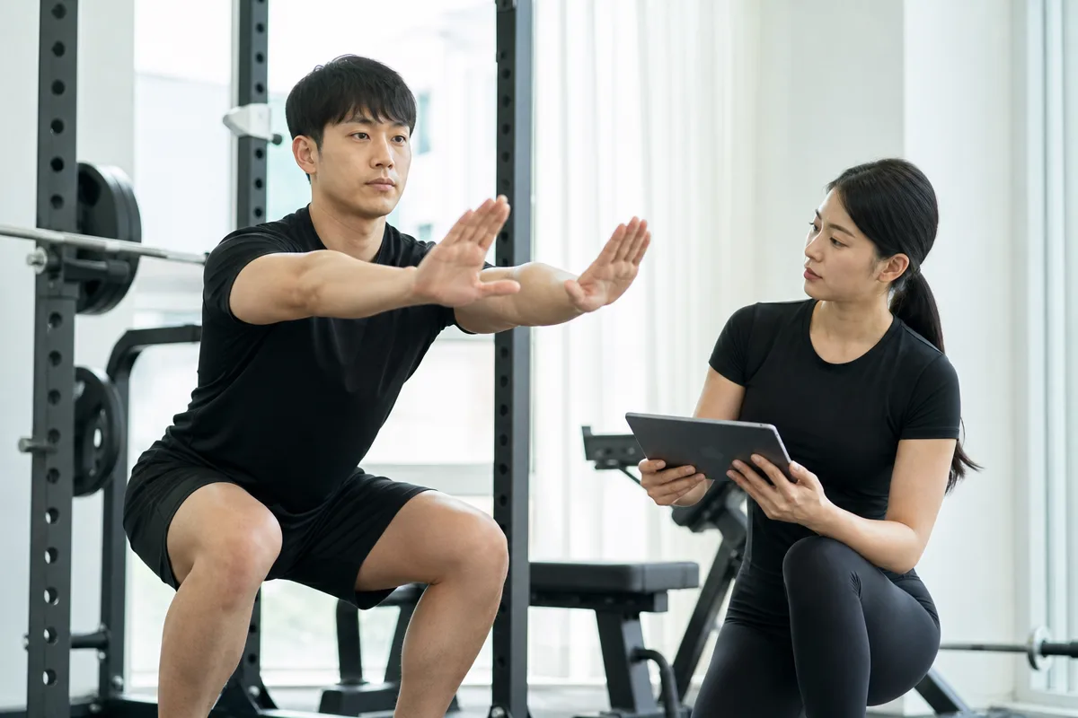 트레이너가 PT 상담 중 회원의 스쿼트 자세와 목표를 확인하는 모습